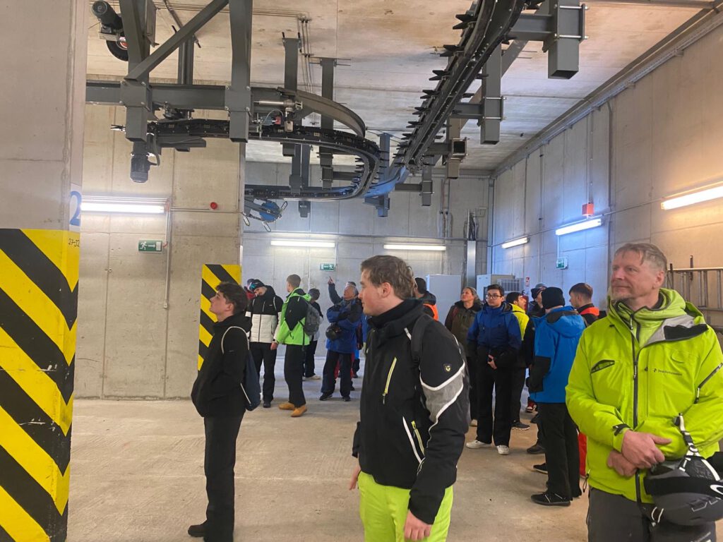Schülerinnen und Schüler besichtigen die Technik im Inneren einer Gondelstation mit Förderanlage unter der Decke.