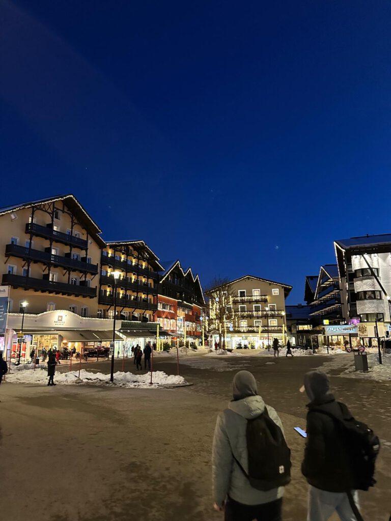 Beleuchtete Häuser im Zentrum von Seefeld in der blauen Abendstunde, im Vordergrund zwei Personen mit Rucksack.